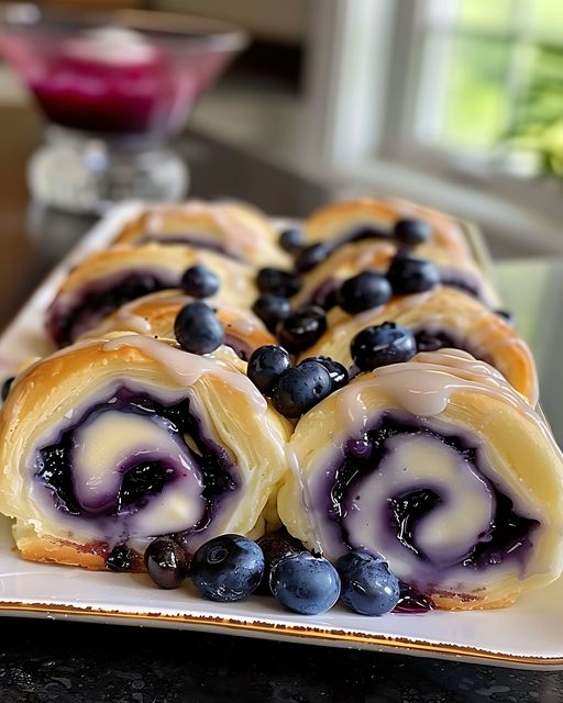 there are blueberries and cream rolls on a plate on a table