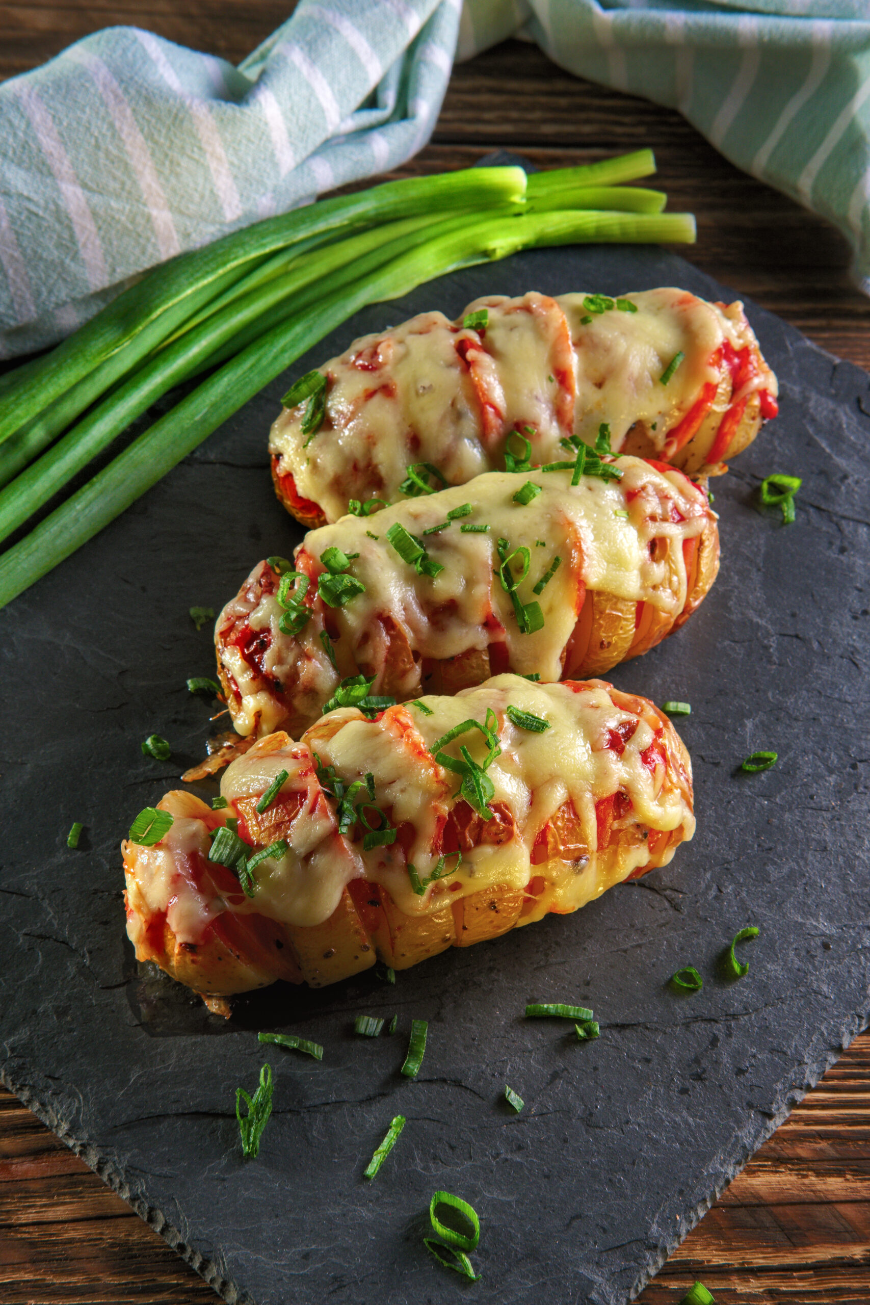 Hasselback potato with chorizo sausage covered with melted cheese baked in oven