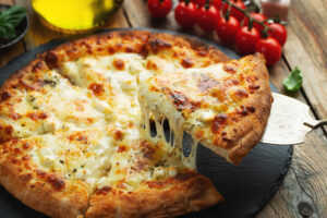 A slice of hot Italian pizza with stretching cheese. Pizza four cheeses with basil on a wooden background.